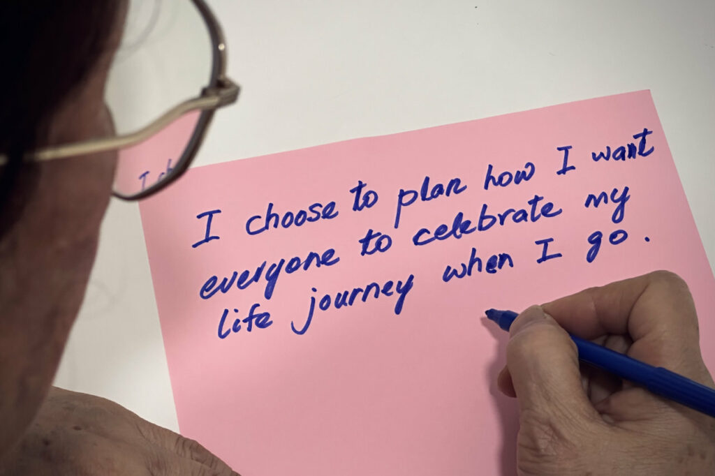 Over shoulder shot of a woman writing on a piece of paper : I choose to plan my funeral because…