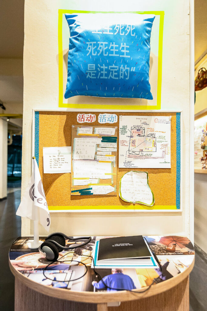 Artwork displayed on a pillar with a pillow, cork board with pinned pieces of paper, a photo booklet and headphone