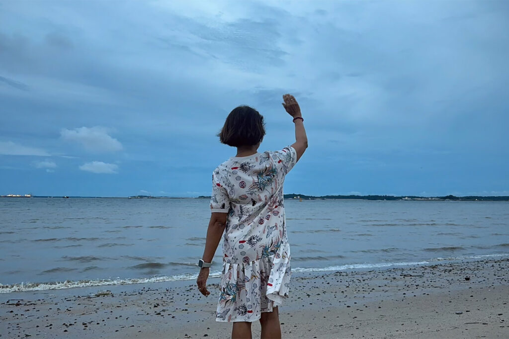 Back view of senior collaborator, Michelle Tan, waving at the sea.