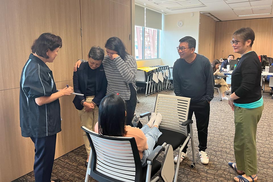 2 facilitators observing a group of 4 workshop participants role play an end of life conversation scenario within a care setting