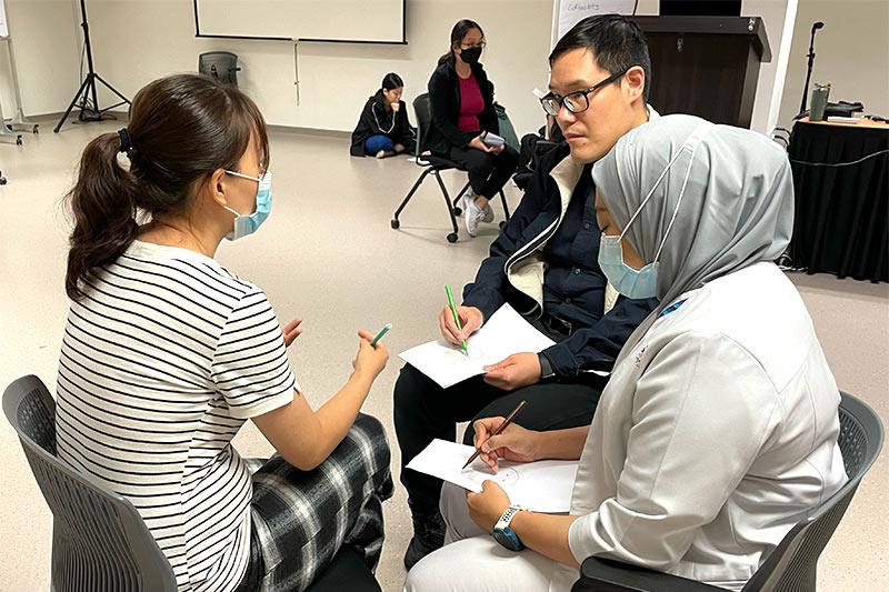 3 healthcare workers seated in deep discussion with pen and paper in their hands